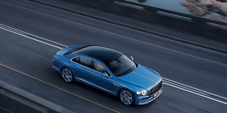 Bentley Casablanca New Bentley Flying Spur Azure sedan in Light windsor blue paint by Mulliner, with 22 inch Azure wheels seen from overhead driving dynamically on a country road