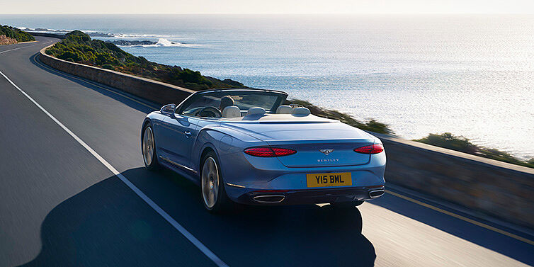 Bentley Casablanca New Bentley Continental GTC Azure convertible rear view in Light Windsor blue paint with 22 inch ten spoke wheels driving dynamically on an ocean road in the sunshine