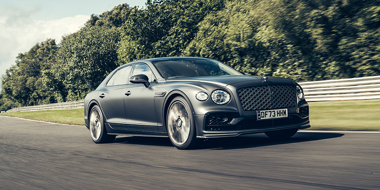 Bentley Casablanca Bentley Flying Spur Mulliner sedan front three quarter in dark grey paint driving dynamically by some trees on a track
