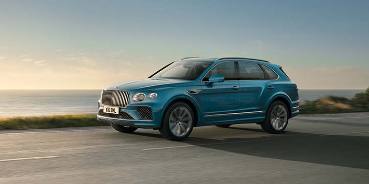 Bentley Casablanca Bentley Bentayga Azure SUV in Topaz blue paint driving dynamically by the ocean with 22 inch 10 spoke directional wheels