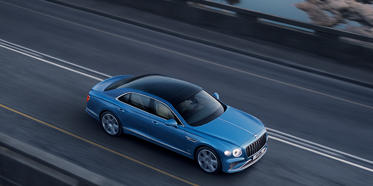 Bentley Casablanca New Bentley Flying Spur Azure sedan in Light windsor blue paint by Mulliner, with 22 inch Azure wheels seen from overhead driving dynamically on a country road