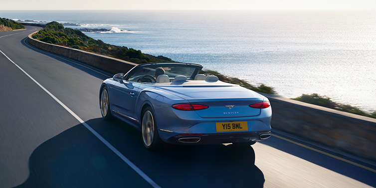 Bentley Casablanca New Bentley Continental GTC Azure convertible rear view in Light Windsor blue paint with 22 inch ten spoke wheels driving dynamically on an ocean road in the sunshine