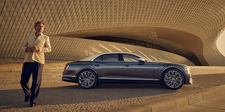 Bentley Casablanca Bentley Flying Spur Mulliner sedan in Rose Gold over Magnetic duotone paint parked by a curved wall with person in suit jacket standing on the left